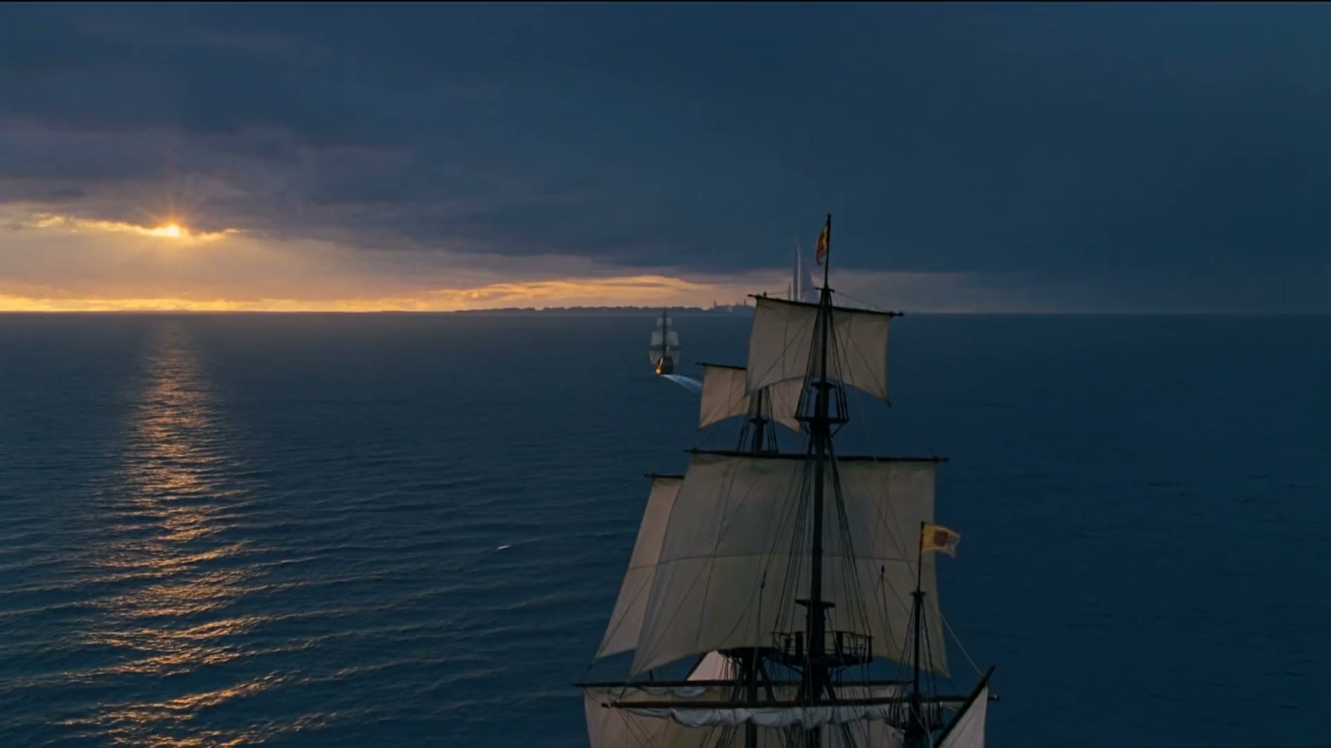 Pasada la tormenta, amanece sobre el mar: el galeón navega hacia una ciudad blanca en el horizonte mientras el sol asoma entre las nubes.